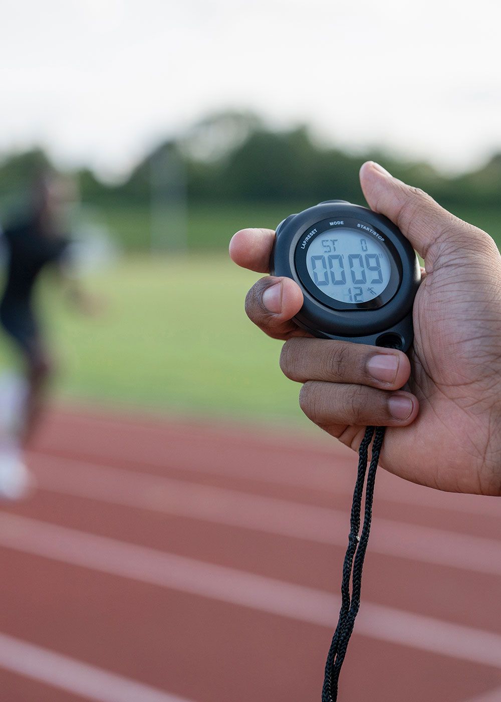 Hand holding a stopwatch beside a running track