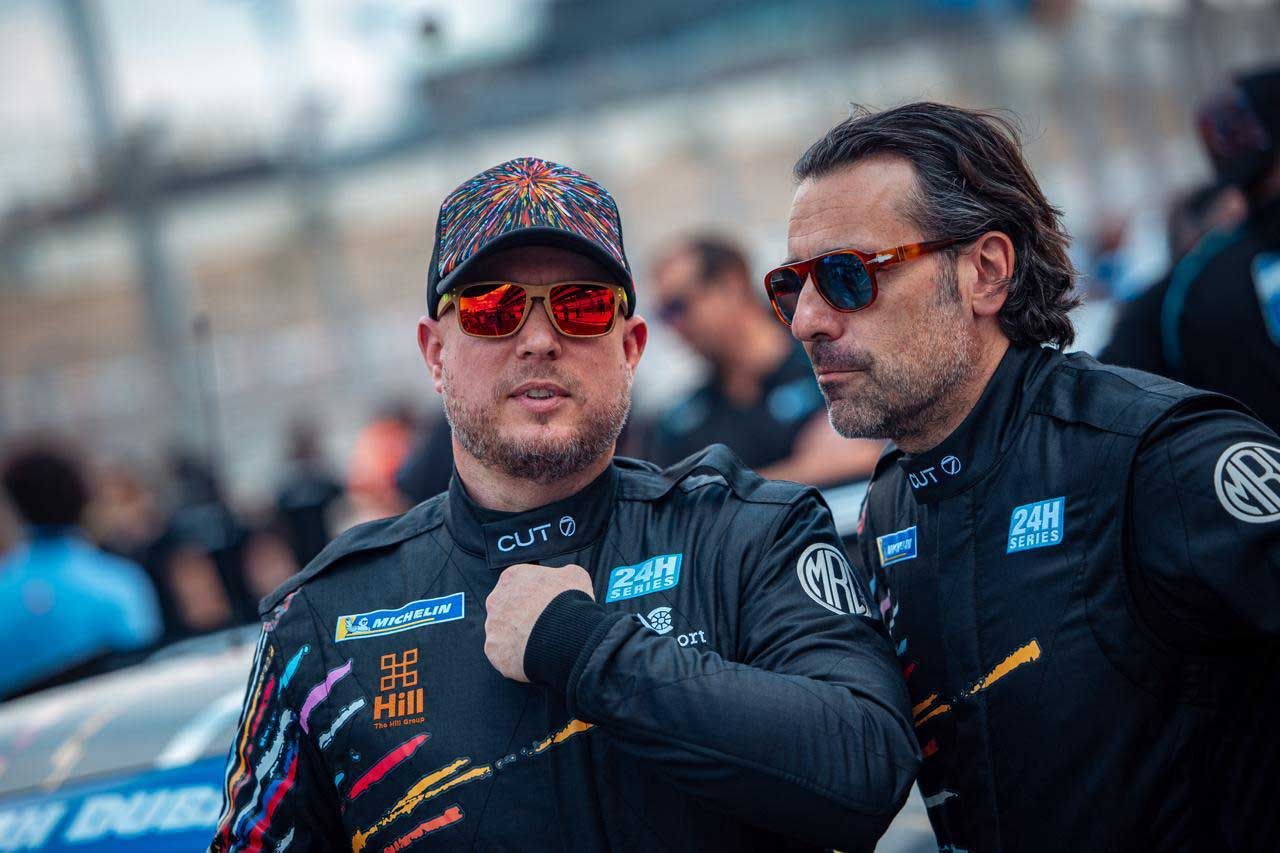 Two drivers in team kit talking in the paddock